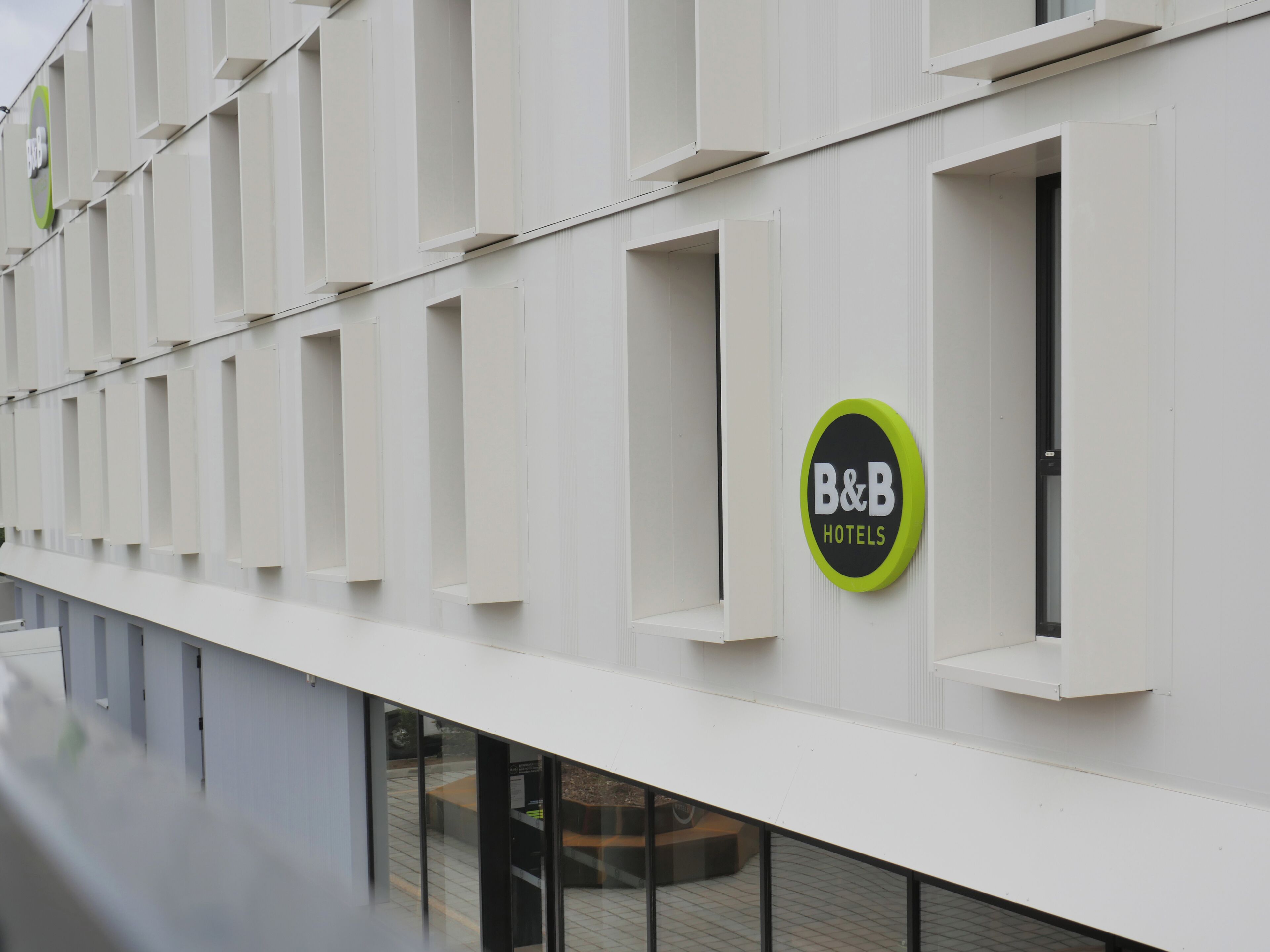 A modern building facade with a series of rectangular windows and a circular sign indicating B&B Hotels.