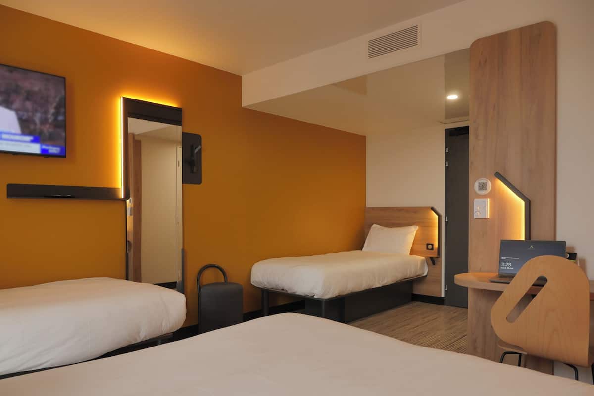 Hotellihuone, jossa on kaksi erillistä sänkyä, työpöytä kannettavalla tietokoneella, tuoli ja seinälle asennettu televisio.