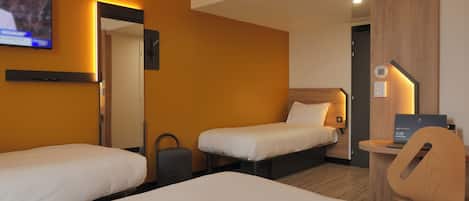 A hotel room with two single beds, a desk with a laptop, a chair, and a TV mounted on the wall.