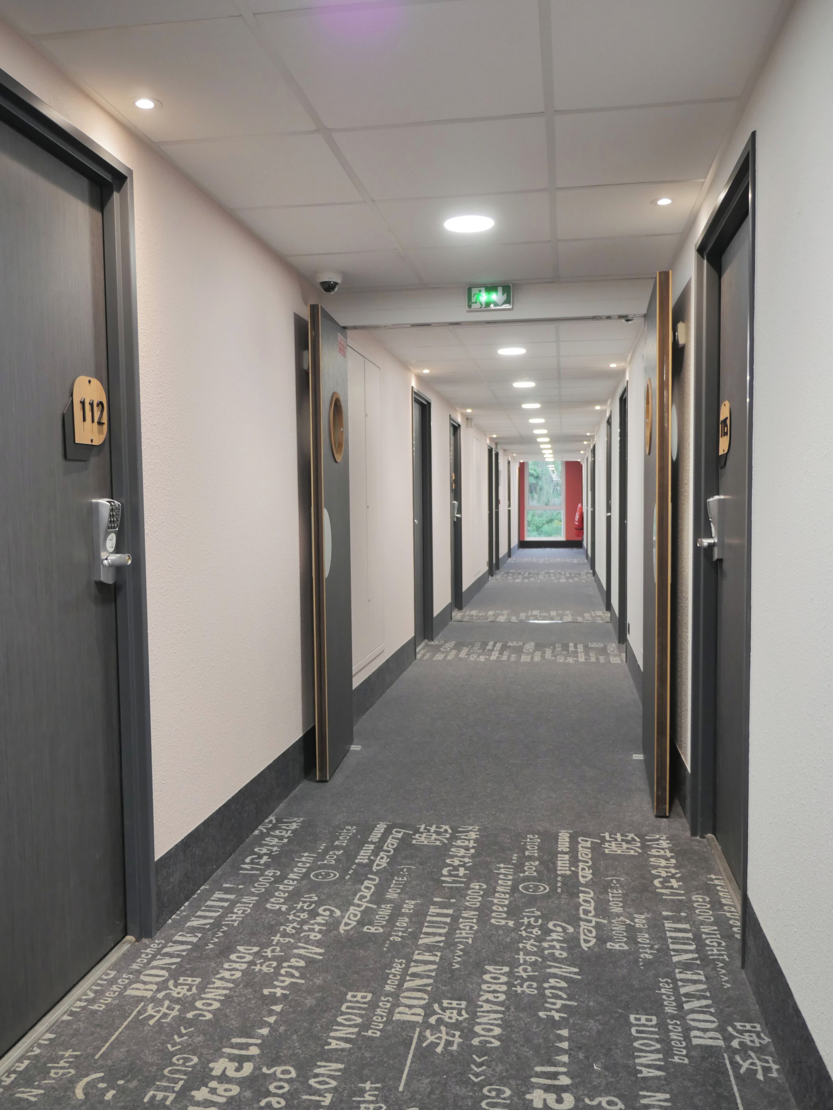 Un pasillo de hotel con puertas numeradas 112 y 113, alfombra estampada e iluminación empotrada.