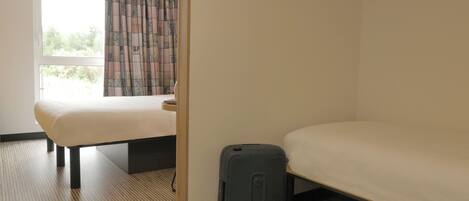 Una habitación de hotel con cama, maleta y ventana con cortinas.