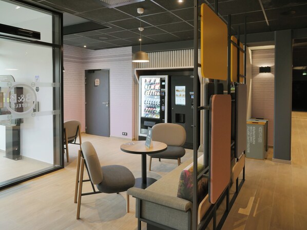 A modern hotel lobby with seating areas, a vending machine, and a glass wall. - B&B HOTEL Carcassonne Rocadest La Cite (Carcassonne)
