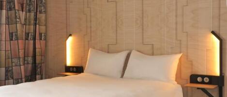 A neatly made bed with a white duvet, two bedside lamps, and a wooden wall with a geometric pattern.