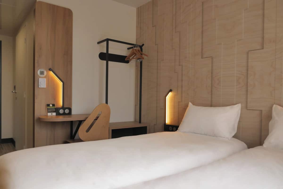 Hotellihuone, jossa on sänky, työpöytä tuolilla ja kaksi yöpöytävalaisinta.