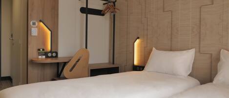 A hotel room with a bed, a desk with a chair, and two bedside lamps.