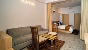 A hotel room with a sofa, a chair, a small table, a bed, and a bathroom visible through an open door. - Devdarshan Hotel And Restaurant (Udaipur)