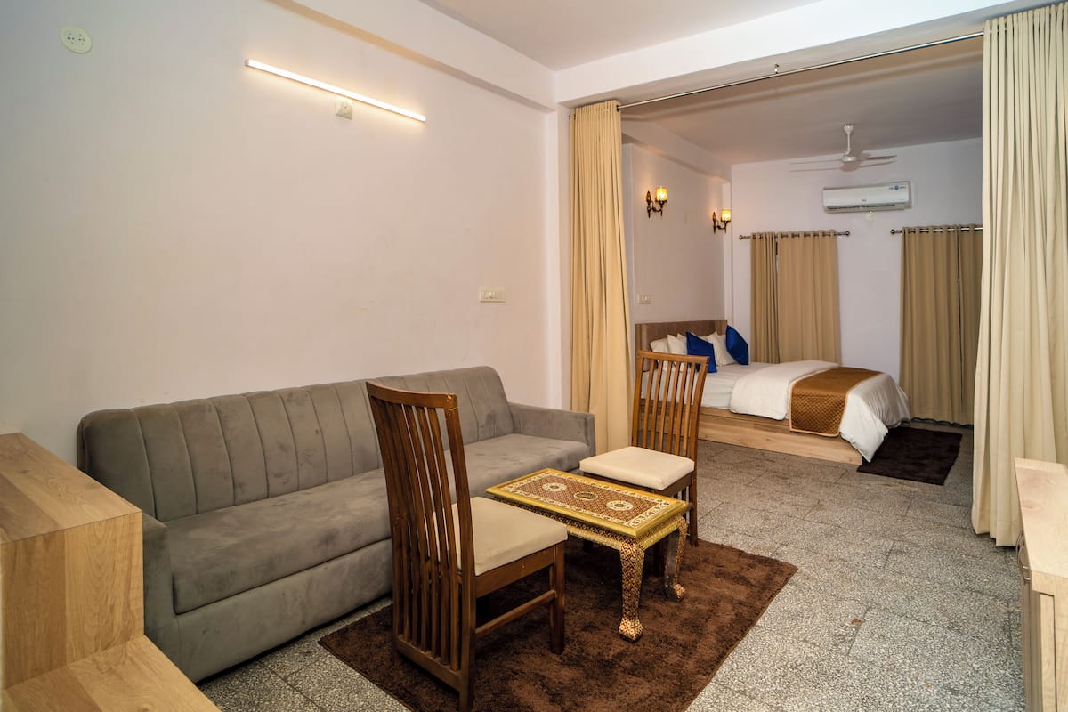 A hotel room with a sofa, a chair, a small table, a bed, and a bathroom visible through an open door.