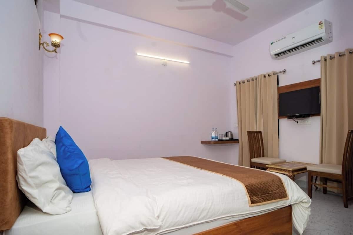 A hotel room with a bed, a desk, a chair, an air conditioner, and a television.