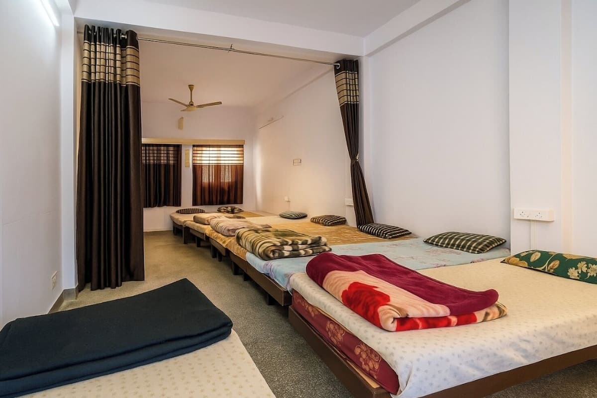 A dormitory room with multiple beds, a ceiling fan, and a window with curtains.