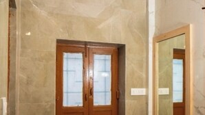 A bathroom with a wooden door, a mirror, and a small wooden bench. - Devdarshan Hotel And Restaurant (Udaipur)