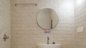 A small bathroom with a white toilet, a pedestal sink, and a round mirror. - Devdarshan Hotel And Restaurant (Udaipur)