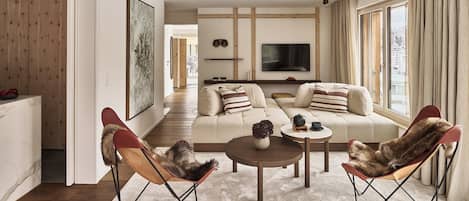 A modern living room with a sofa, two armchairs, a coffee table, and a TV.