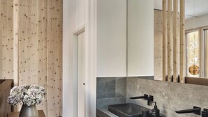 A modern bathroom with a wooden floor, a sink with a black faucet, and a mirror above the sink. - The View (St. Moritz)