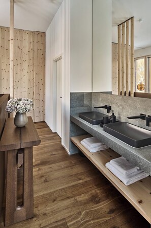 A modern bathroom with a wooden floor, a sink with a black faucet, and a mirror above the sink. - The View (St. Moritz)