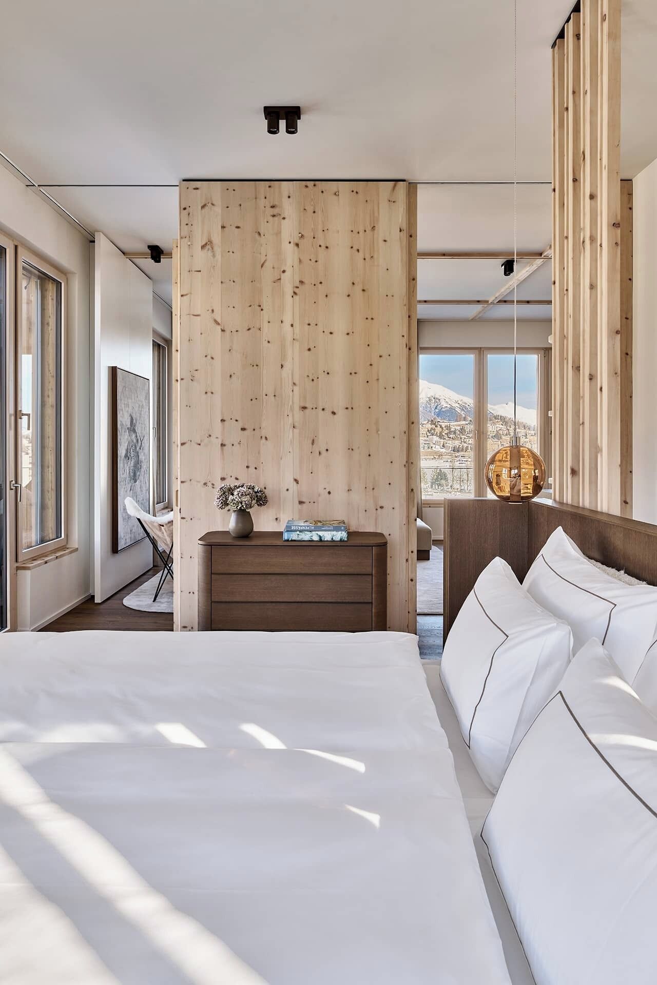 Un dormitorio moderno con una cama grande, cabecera de madera y vistas a una montaña nevada.