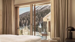 A hotel room with a large window offering a view of a snowy mountain and forest. - The View (St. Moritz)
