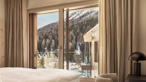 A hotel room with a large window offering a view of a snowy mountain and forest. - The View (St. Moritz)