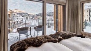 A hotel room with a large window offering a view of a snowy mountain and a cityscape. - The View (St. Moritz)