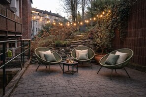 Un patio al aire libre con sillas de mimbre, una mesa pequeña y luces colgantes.