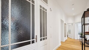 Un pasillo con piso de madera, paredes blancas y una puerta con paneles de vidrio esmerilado.