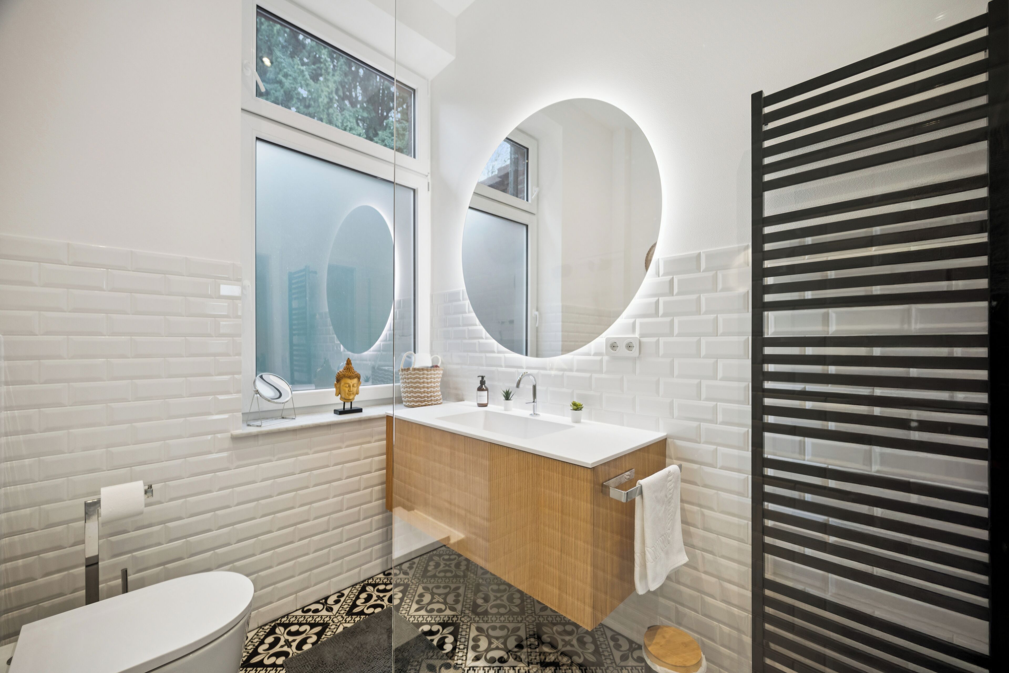Un bagno moderno con parete in mattoni bianchi, mobile lavabo in legno, specchio rotondo e water.