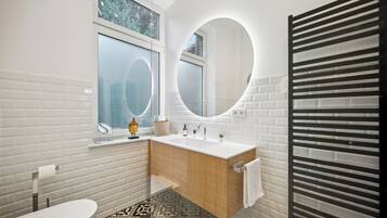 A modern bathroom with a white brick wall, a wooden vanity, a round mirror, and a toilet.