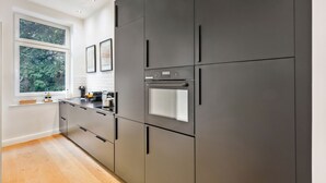 Una cocina moderna con armarios oscuros, una ventana con vista a la vegetación y un horno empotrado.