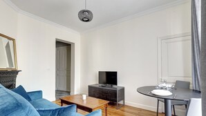 A modern living room with a blue sofa, a wooden coffee table, a dark cabinet with a flat-screen TV, and a dining table set for two.