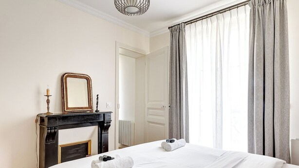 A hotel room with a bed, a fireplace, a mirror, and a window with curtains.