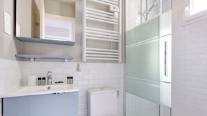 A modern bathroom with a glass shower enclosure, a white toilet, and a vanity with a mirror and towel rack.