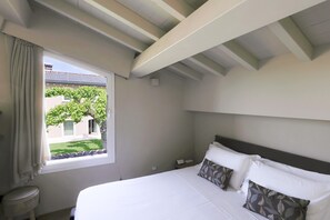 Une chambre à coucher avec un lit, une fenêtre avec des rideaux, une vue sur un immeuble et un arbre, et un plafond blanc.