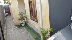 A narrow outdoor corridor with a paved path, potted plants, and a vehicle parked on the right.
