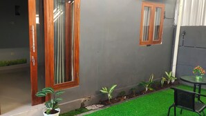 A modern outdoor area with a glass door leading to a room, a small garden with potted plants, and a round table with chairs.