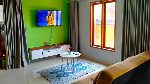 A modern living room with a green wall, a flat-screen TV, a sofa, a coffee table, and a window with curtains.