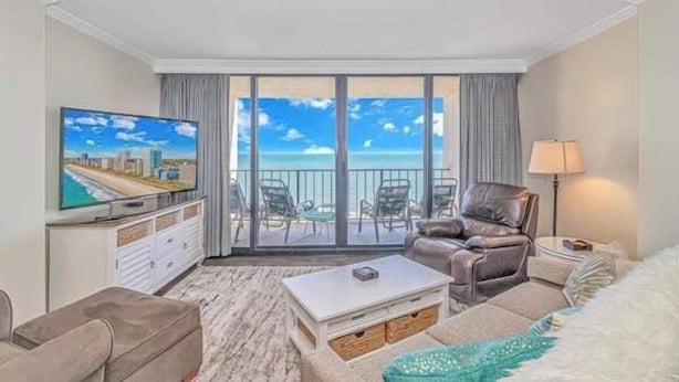 Une chambre d’hôtel avec un balcon, une télévision, un canapé, une table basse et une lampe.