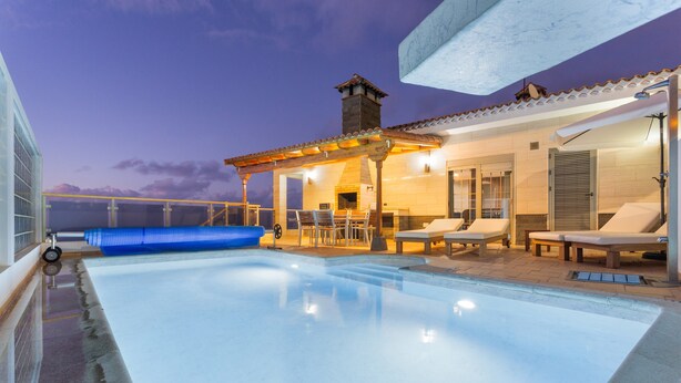 Ein Schwimmbecken mit Liegestühlen und einer überdachten Terrasse.
