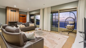 Ein modernes Wohnzimmer mit einer Couch, einem Couchtisch und einem Fernseher. Ein Balkon bietet Blick aufs Meer.