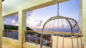 Ein Balkon mit Hängesessel, Glasgeländer und Meerblick.