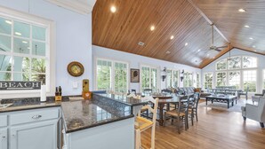 A spacious kitchen with a large island, wooden ceiling, and large windows offering views of the outdoors. - Oceans Rest Private Pool, luxury living in DeBordieu 7 bedrooms (Georgetown)