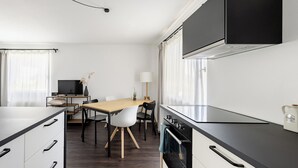 Een moderne keuken met een zwart aanrecht, witte kasten, een houten eettafel en een aan de muur bevestigde televisie.