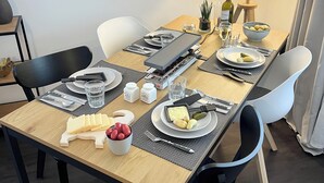 Een eettafel gedekt met borden, bestek en toevoegingen, omringd door stoelen.