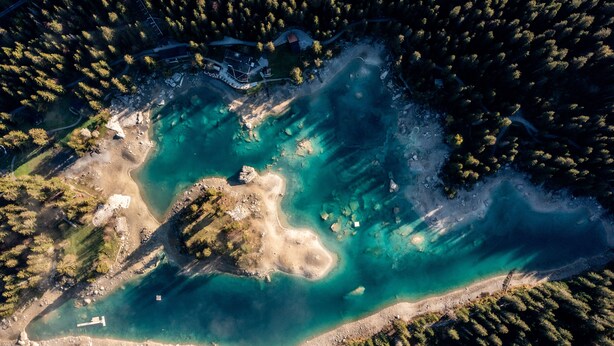 Luchtbeeld van een kustgebied met helder turquoise water, een zandstrand en dichtbegroeide bosgebieden.