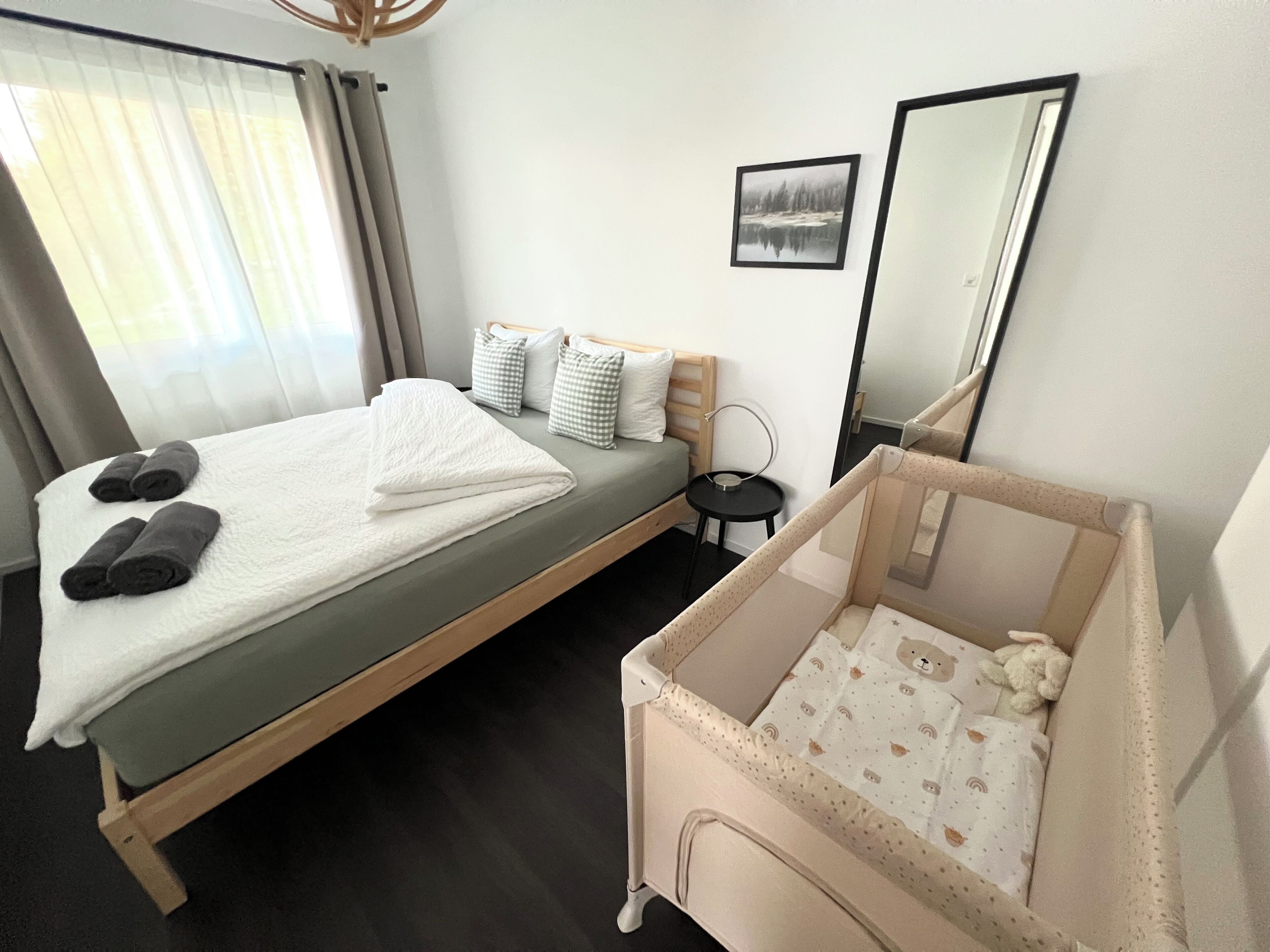 Ein Hotelzimmer mit einem Bett, einem kleinen Nachttisch, einem Babybett, einem Spiegel und einem Bild an der Wand.