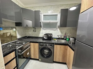A compact kitchen with a gas stove, a built-in washing machine, and a stainless steel refrigerator.