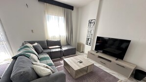 Ein modernes Wohnzimmer mit grauem Sofa, Couchtisch, Flachbildfernseher und Heizkörper.