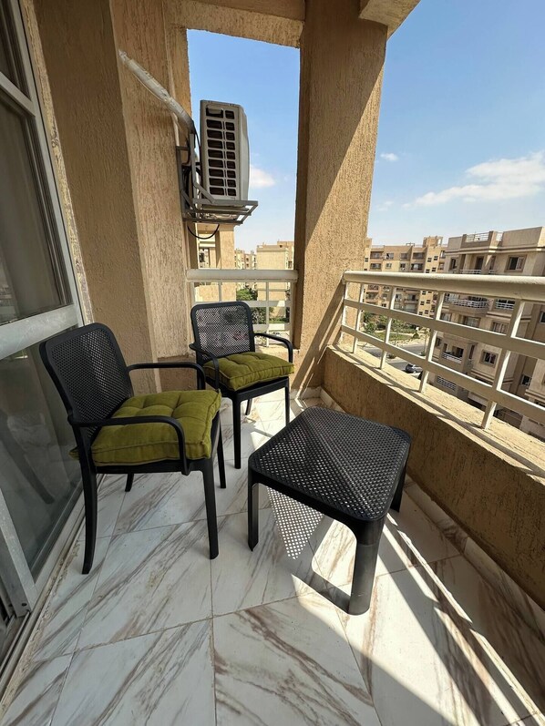 A balcony with two chairs and a small table, an air conditioning unit, and a view of residential buildings.