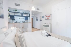 Une chambre moderne avec un lit, un bureau et un coin cuisine en arrière-plan.