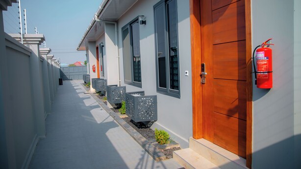 A corridor with doors on the right, a fire extinguisher on the wall, and a row of planters along the path. - Staycation Villas (Dodoma)