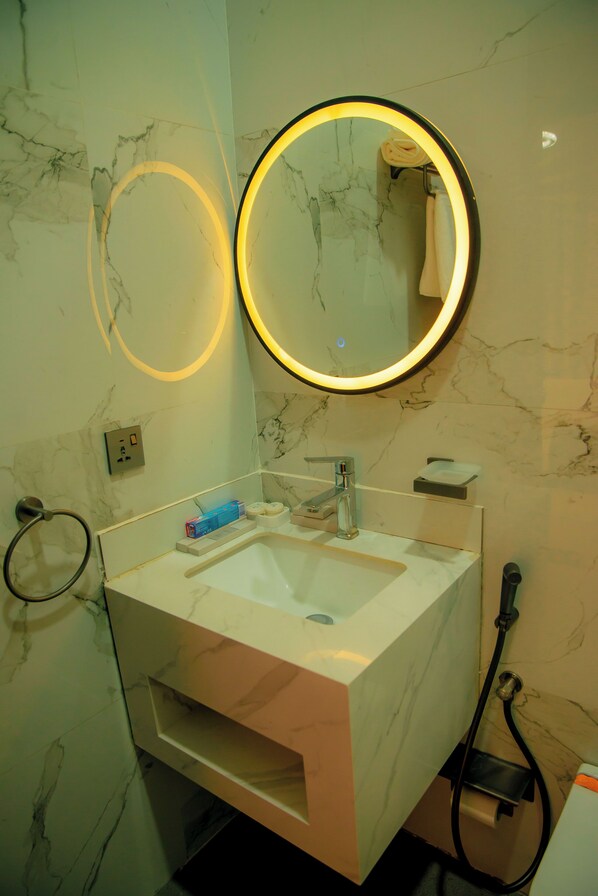 A bathroom with a marble sink, a round mirror with a light, and a towel rack.