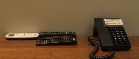 A desk with a white scale, two black remote controls, and a black telephone with a service label.